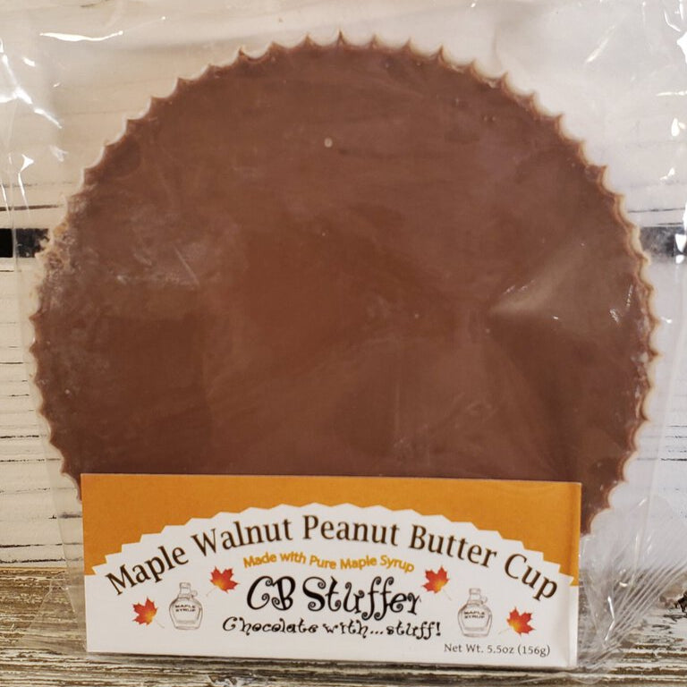 A large chocolate peanut butter cup with visible pieces of nuts, wrapped in clear packaging with a label reading 'Maple Walnut Peanut Butter Cup'.