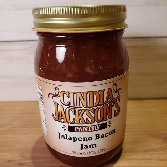 Jar of Cindia Jackson's Pantry Jalapeno Bacon Jam on a wooden surface with a white background