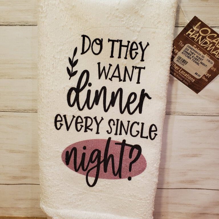 A white kitchen towel with black printed text and a decorative element, displayed on a wooden surface, with a brown 'Local Handmade' tag attached to it.