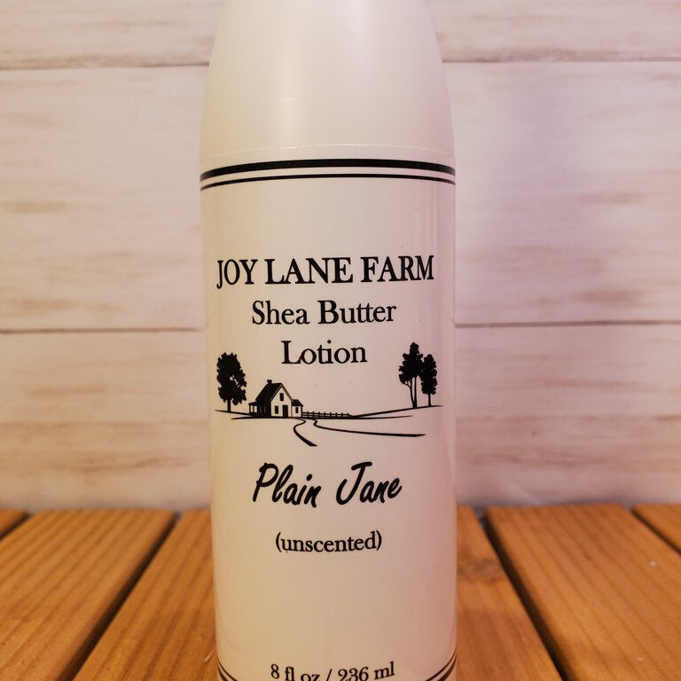 Shea butter lotion bottle labeled 'Plain Jane' from Joy Lane Farm on a wooden surface.