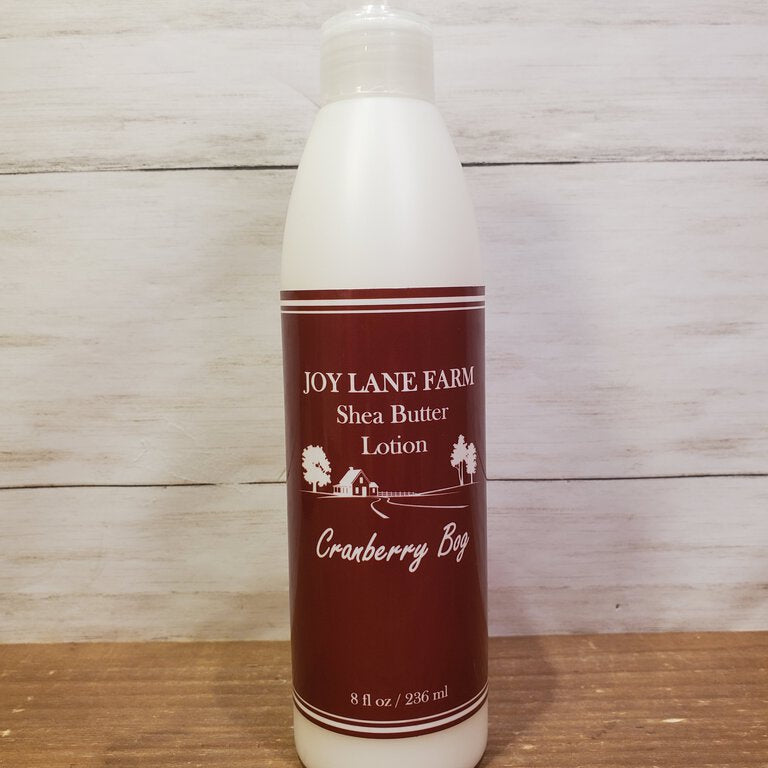 A pump bottle of Cranberry Bog Shea Butter Lotion from Joy Lane Farm, placed on a wooden surface.