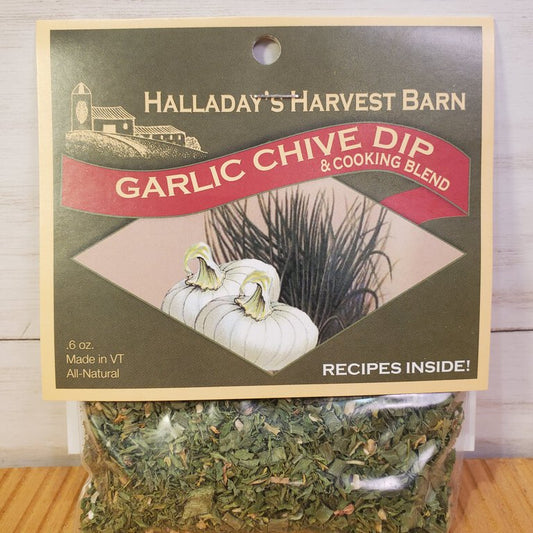 Packaging of Garlic Chive Herb Dip & Cooking Blend from Halladay's Harvest Barn featuring an image of the dip container with a green label, some chives, and a white flower, against a wooden background.
