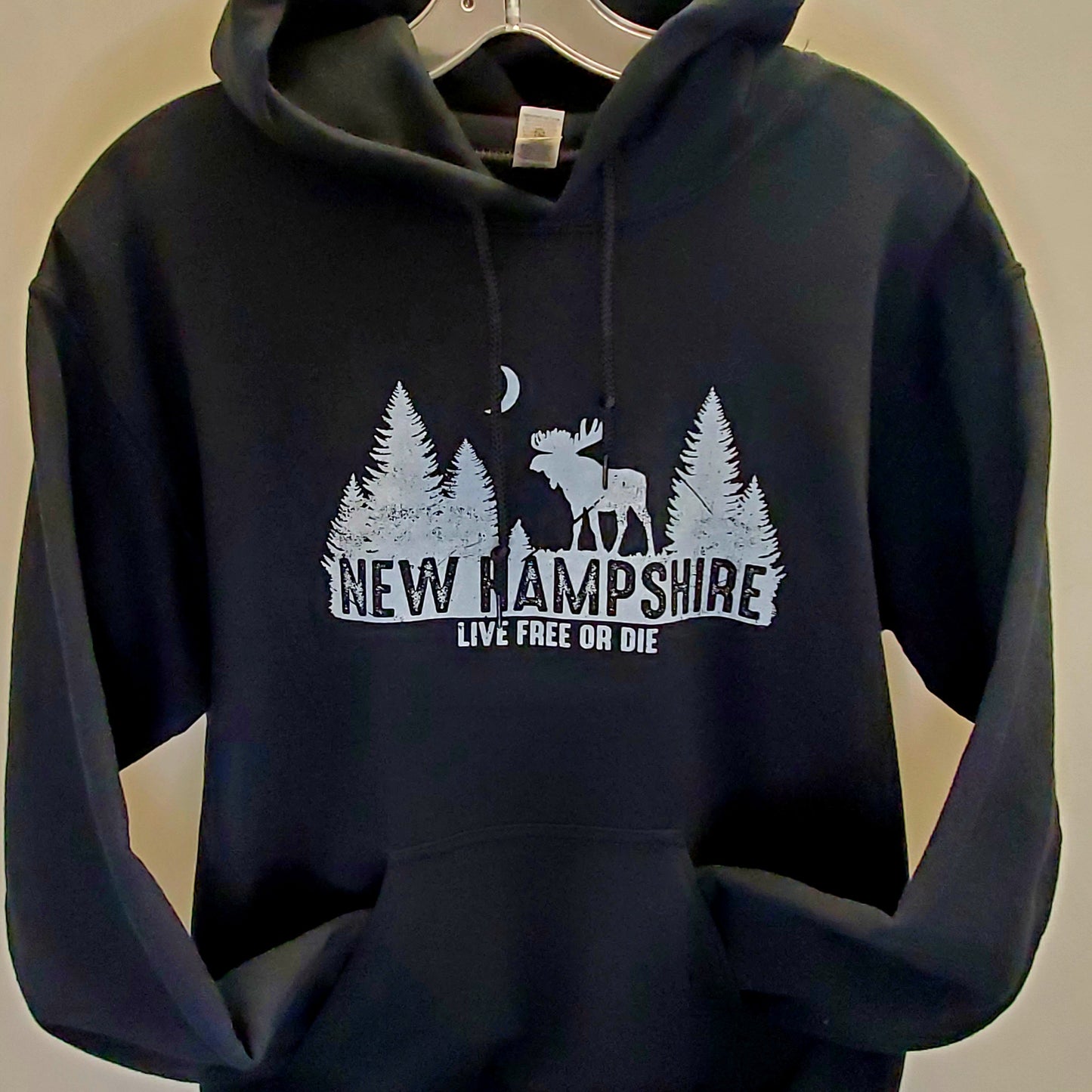 Black hoodie with New Hampshire design on a hanger against a beige background
