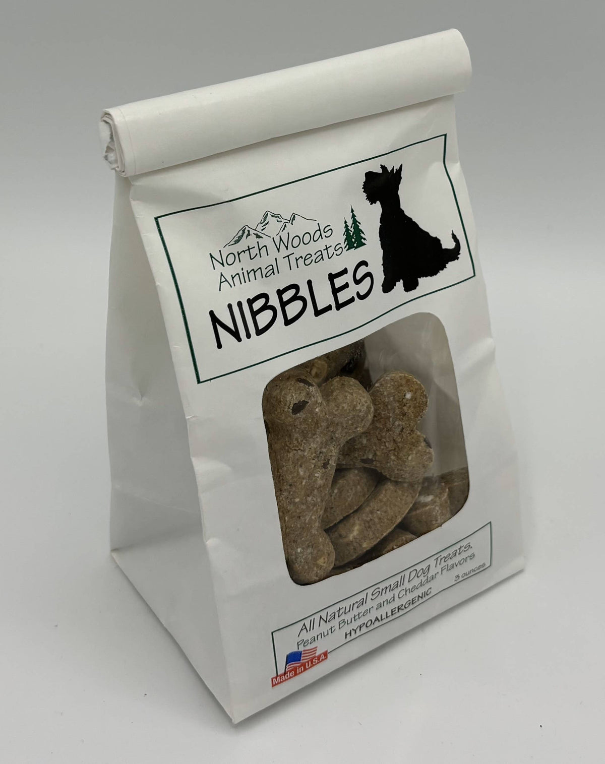 A white stand-up paper bag of North Woods Animal Treats Nibbles dog treats, featuring a clear window that displays the brown bone-shaped treats inside.