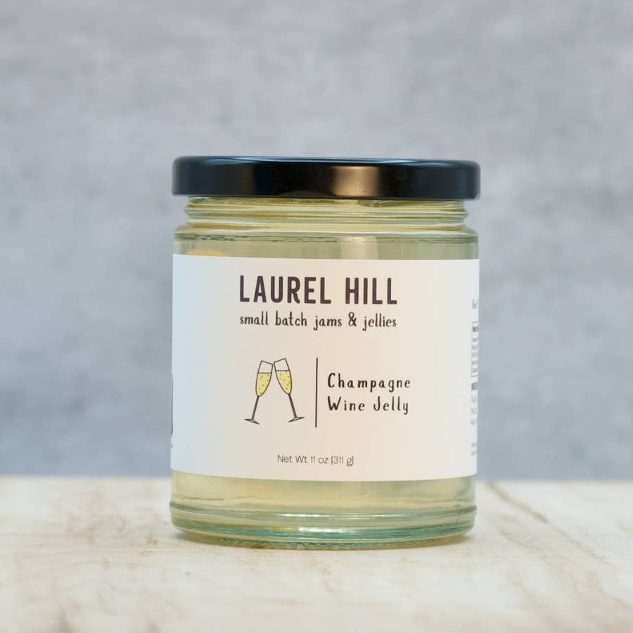 A jar of Laurel Hill Small Batch Jams & Jellies, specifically Champagne Wine Jelly, with a white label and black lid, set on a light marble surface against a gray background.