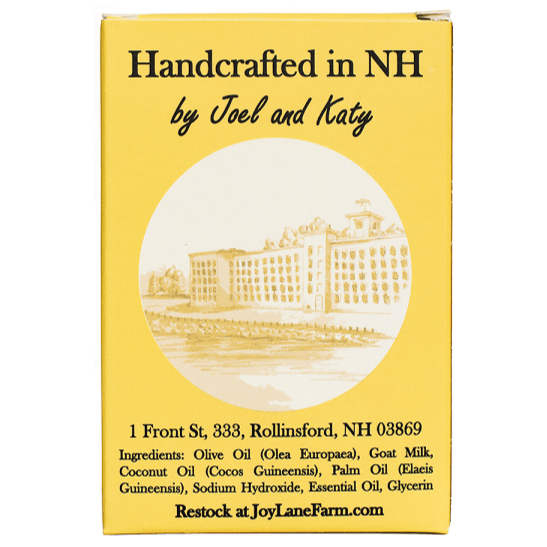 A yellow rectangular box with black text reading 'Handcrafted in NH by Joel and Katy' and a sepia illustration of a building in a circular inset. The box also includes an address and ingredient list, plus 'Restock at JoyLaneFarm.