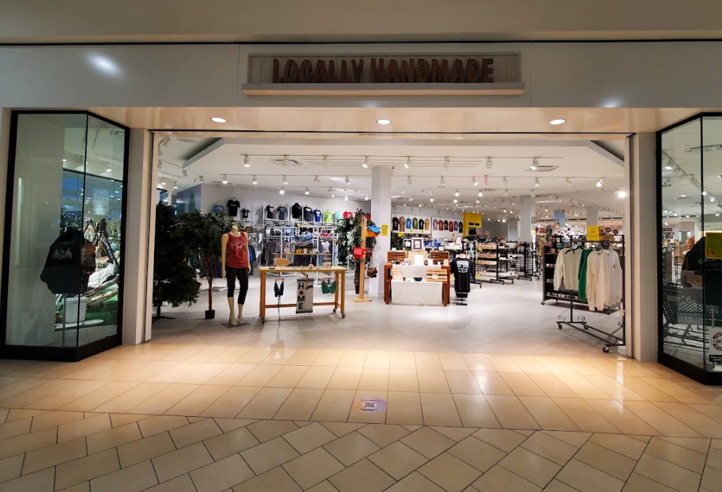 Storefront with 'Locally Handmade' sign, displaying clothing and accessories.