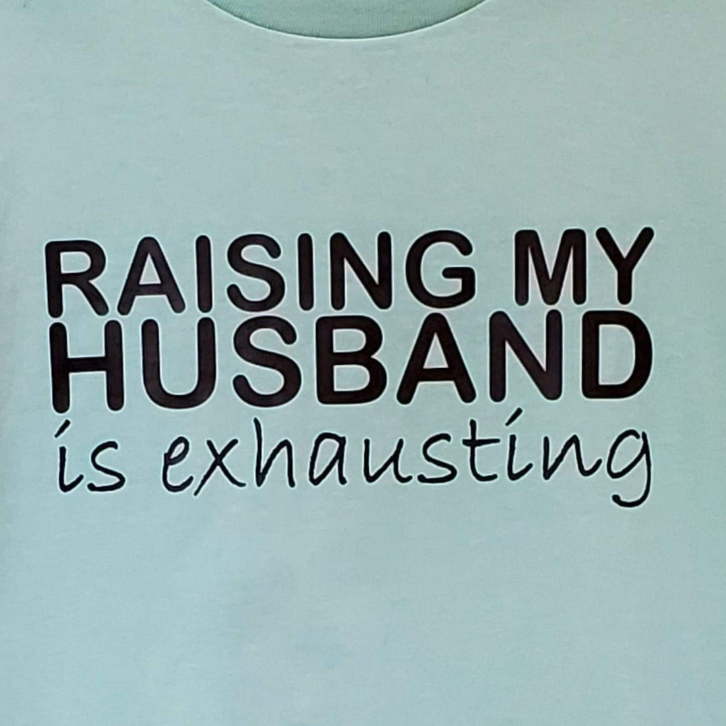 Light blue t-shirt with text 'RAISING MY HUSBAND is exhausting' on a light blue background