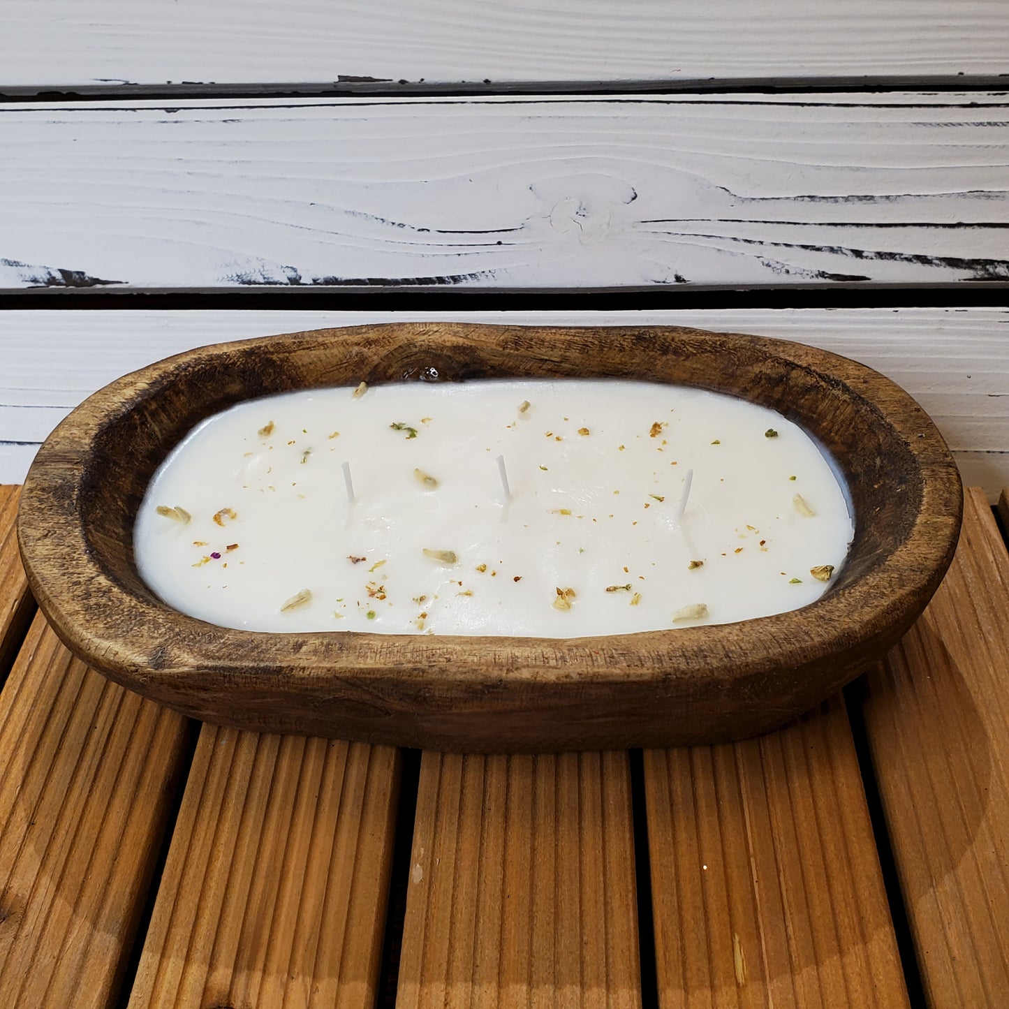 White candle with gold flecks in a wooden bowl on a wooden surface