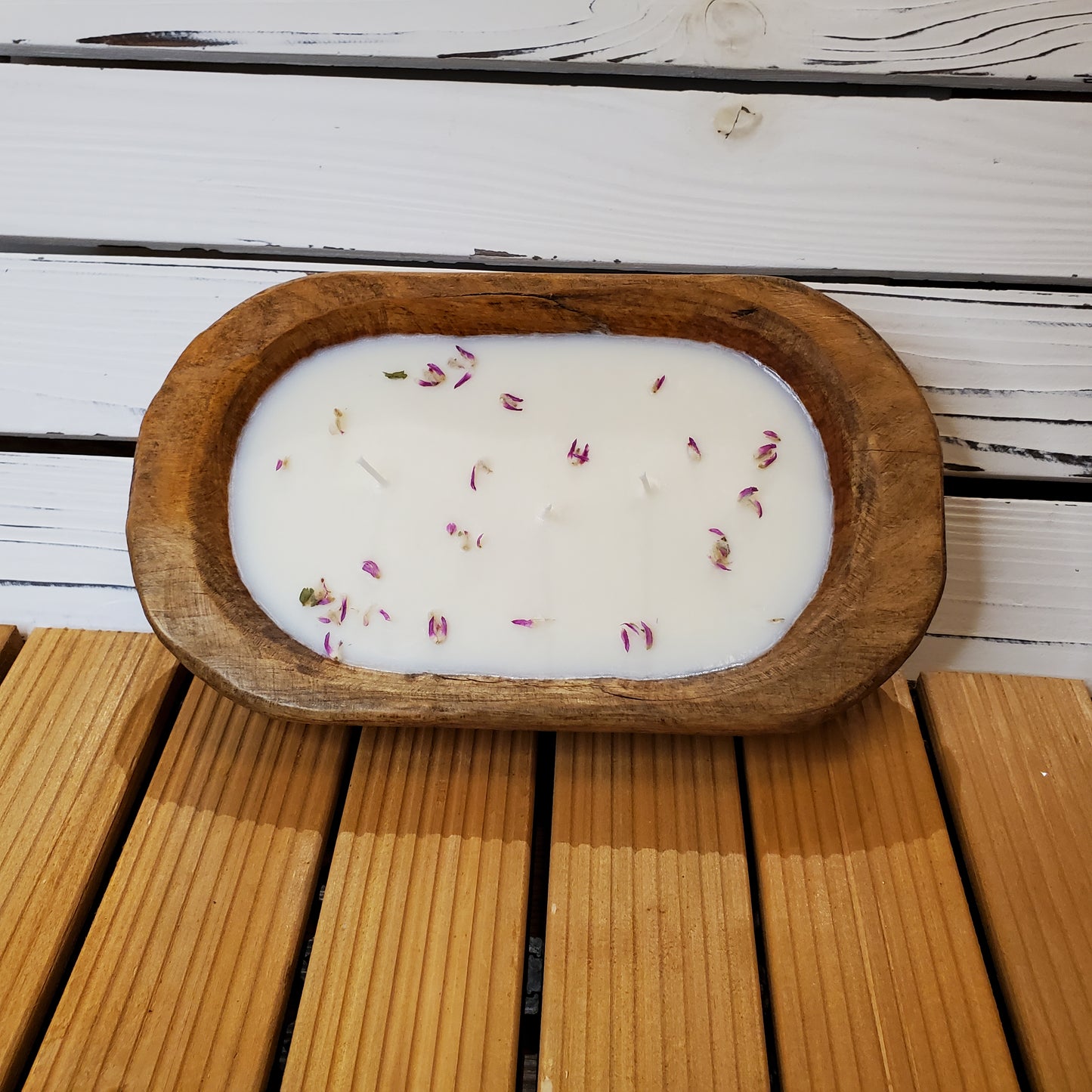 Wooden dish with a white candle and rose petals on a wooden surface