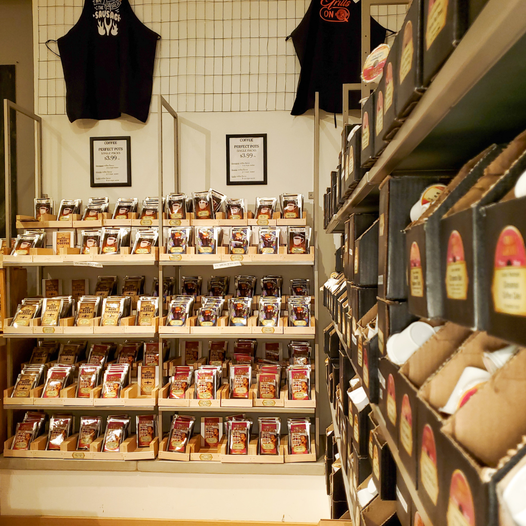 Store interior with shelves displaying packaged goods and hanging clothing.