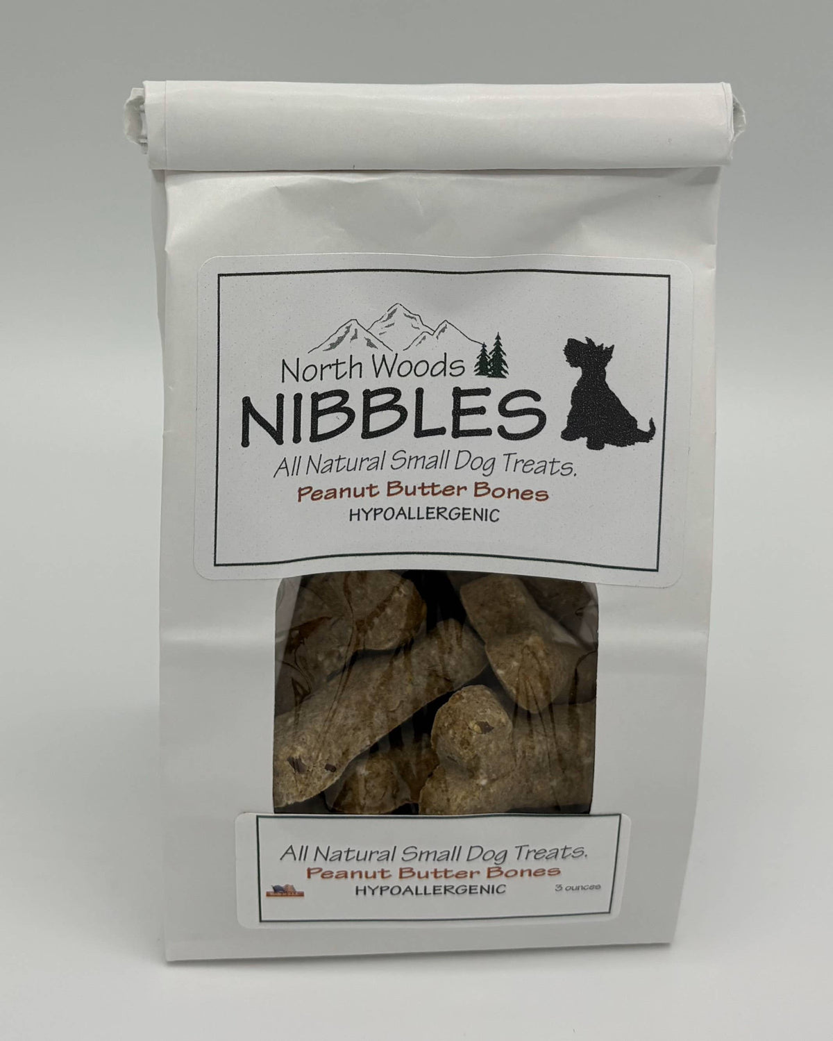 A white stand-up pouch of North Woods Nibbles All Natural Small Dog Treats, Peanut Butter Bones, with a clear window showing the brown treat pieces inside.