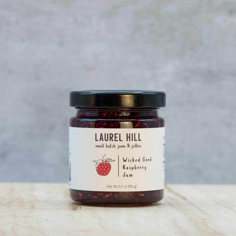 Jar of Laurel Hill Wicked Good Raspberry Jam on a wooden surface with a gray background