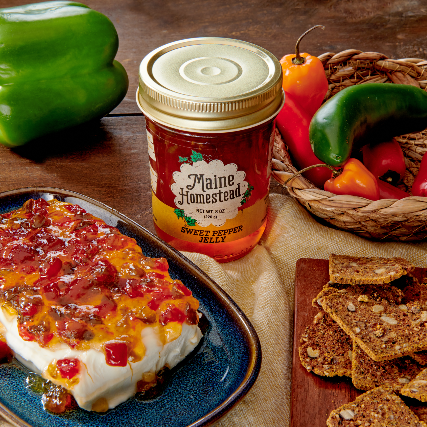 Jar of Maine Homestead Sweet Pepper Jelly on a plate with crackers and peppers