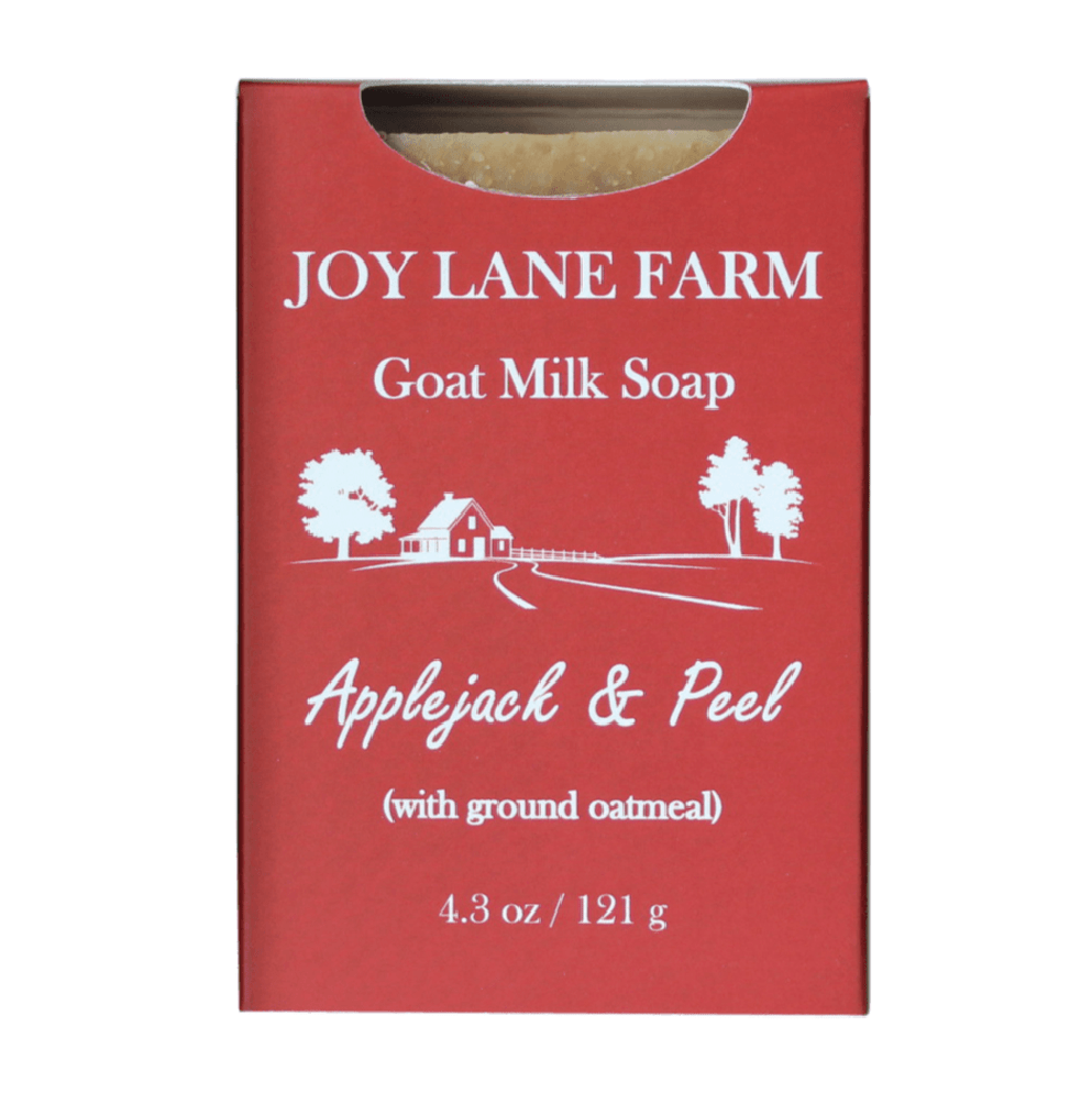 A red rectangular box of Joy Lane Farm Goat Milk Soap, Applejack & Peel variant, with white text and a small illustration of a farm scene. A small cutout at the top reveals a bar of soap inside.