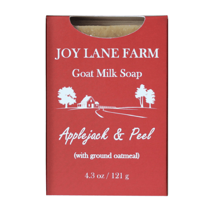 A red rectangular box of Joy Lane Farm Goat Milk Soap, Applejack & Peel variant, with white text and a small illustration of a farm scene. A small cutout at the top reveals a bar of soap inside.