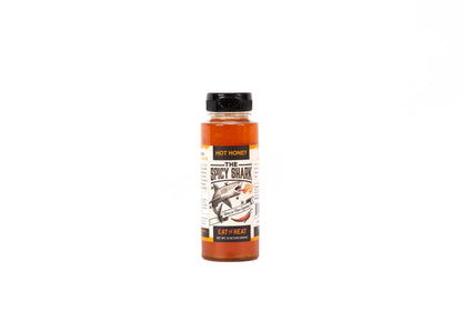 A bottle of 'The Spicy Shark' hot sauce by Hot Honey, featuring a black cap and a label with a shark illustration, set against a plain white background.
