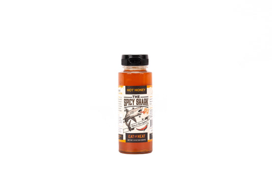 A bottle of 'The Spicy Shark' hot sauce by Hot Honey, featuring a black cap and a label with a shark illustration, set against a plain white background.