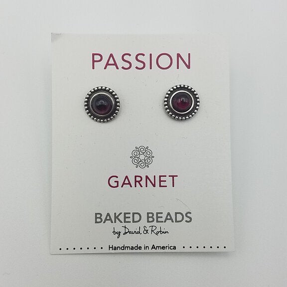 A pair of garnet power stone stud earrings displayed on a white card with 'PASSION GARNET' written on it, under the brand name 'BAKED BEADS by Joshua & Rachel'.