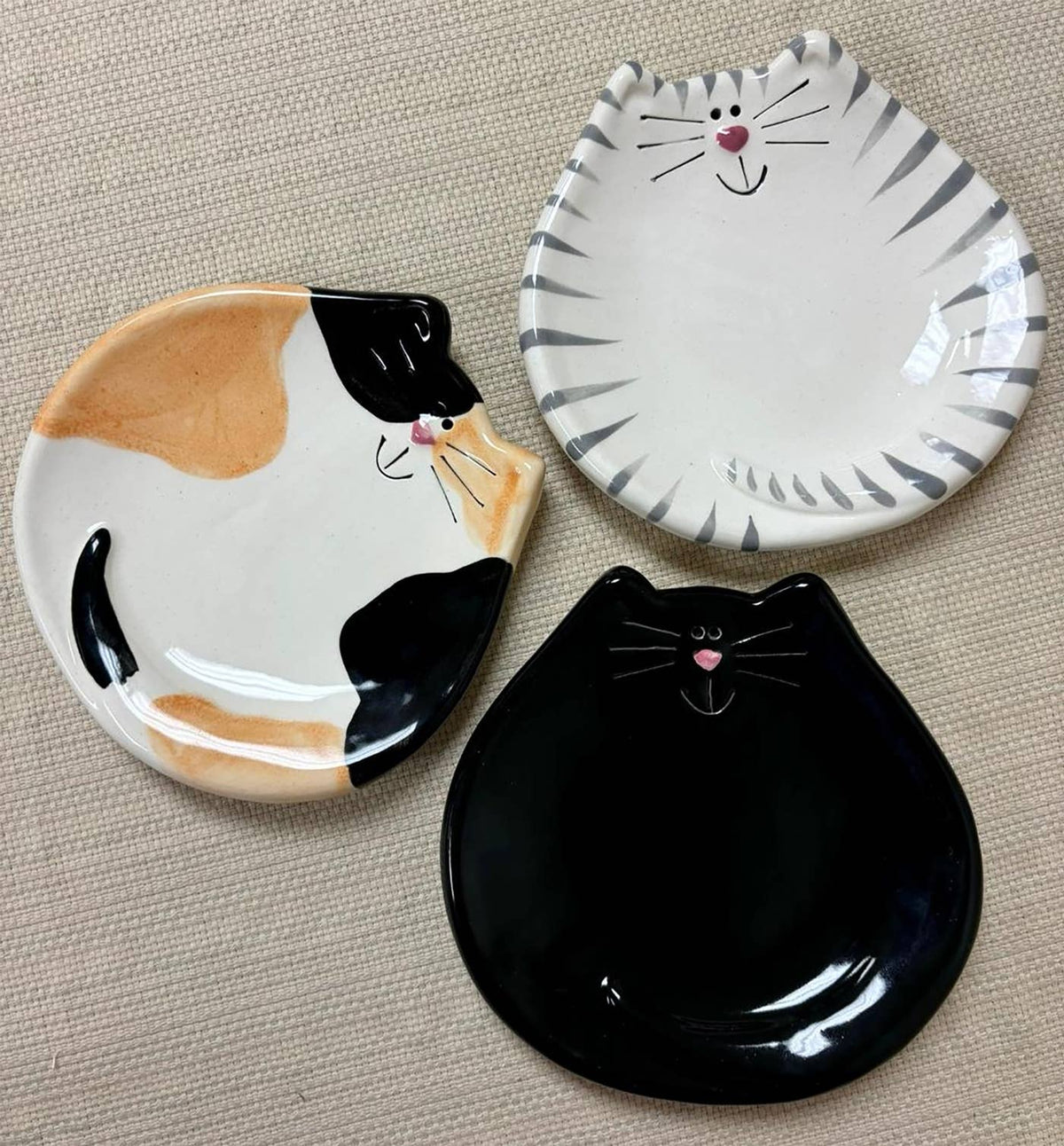 Three ceramic cat-shaped plates on a textured surface