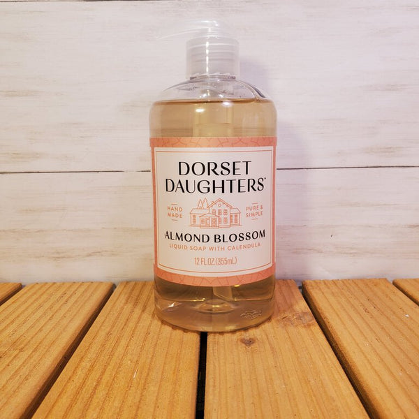 A clear plastic bottle of Almond Blossom Liquid Soap by Dorset Daughters, placed on a wooden surface.