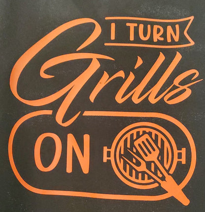 Black apron with orange text that reads 'I TURN Grills ON' with a grill and fork graphic