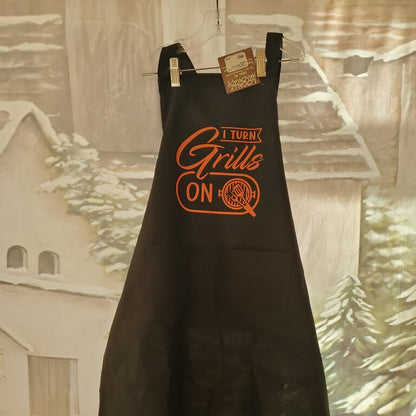 A black apron with the text 'I Turn Grills On' printed in orange.