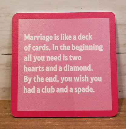 A red square coaster with white text that reads: 'Marriage is like a deck of cards. In the beginning all you need is two hearts and a diamond.