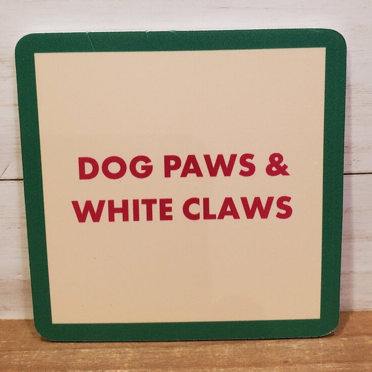A square coaster with green trim and a beige center, text on the coaster reads 'DOG PAWS & WHITE CLAWS'.