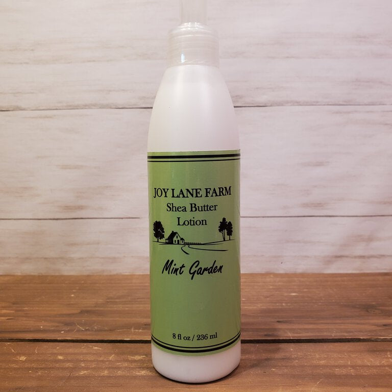 Bottle of Joy Lane Farm Shea Butter Lotion on a wooden surface with a wooden background