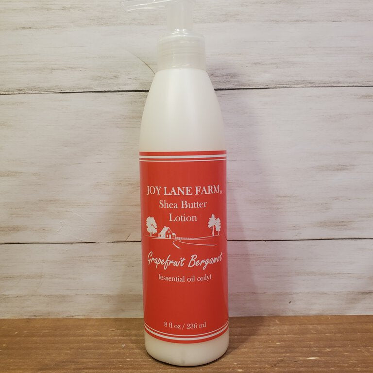 A bottle of Grapefruit Bergamot Shea Butter Lotion from Joy Lane Farm, with a white label and red text on a wooden background.