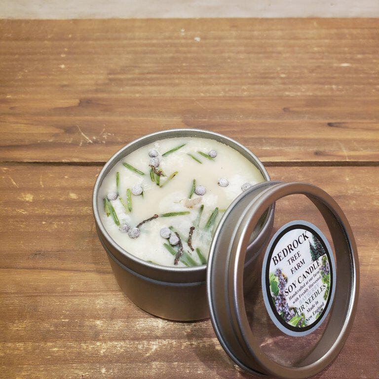 A tin candle with a clear window top, featuring a bayberry candle inside, placed on a wooden surface.