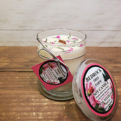 A clear glass jar candle with a white soy wax melt, adorned with pink and purple flowers and a label that reads 'BEACH ROSE', alongside its lid with additional product information.