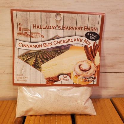 Packaging of Cinnamon Bun Cheesecake Mix on a wooden surface. The package is primarily beige and brown with an image of a cinnamon roll and a cheesecake on the front.