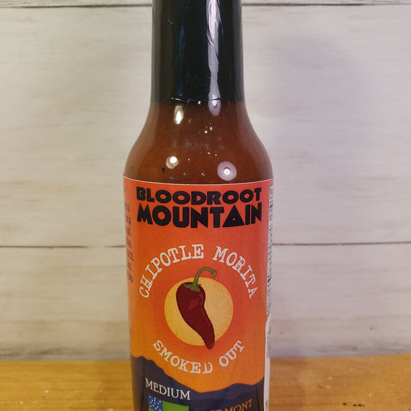 A bottle of Bloodroot Mountain Chipotle Morita Hot Sauce on a wooden surface.