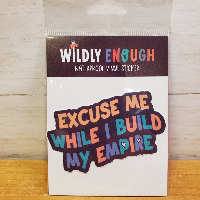 A sticker with the phrase 'Excuse Me While I Build My Empire' printed in multicolored letters, packaged on a card.