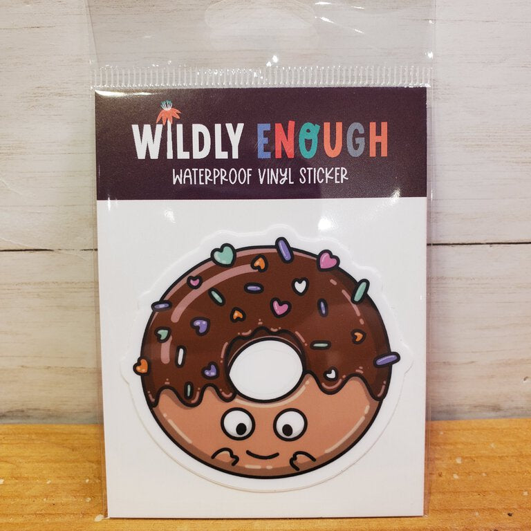 A vinyl sticker depicting a chocolate donut with sprinkles, packaged in a clear plastic sleeve with the brand 'Wildly Enough' printed at the top.