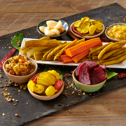 Assorted pickled vegetables on a dark slate surface with a wooden background