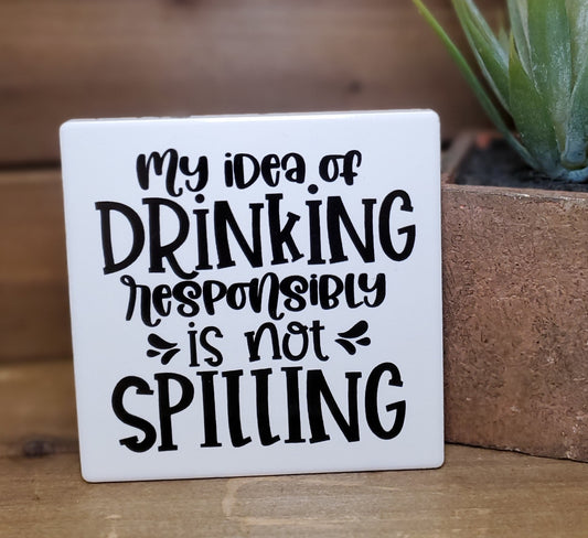 White sign with black text 'My idea of drinking responsibly is not spilling' on a wooden surface.