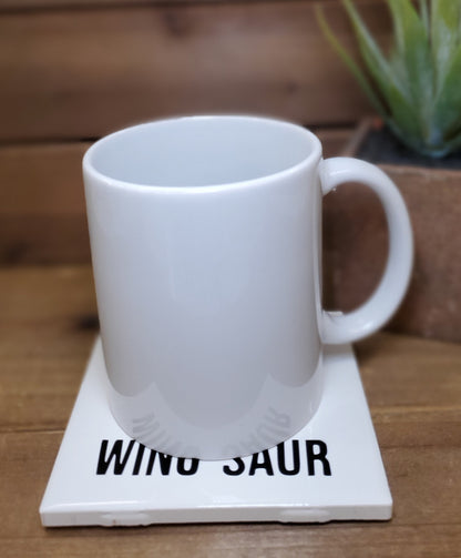 White mug on a coaster with 'Wino Saur' text on a wooden surface