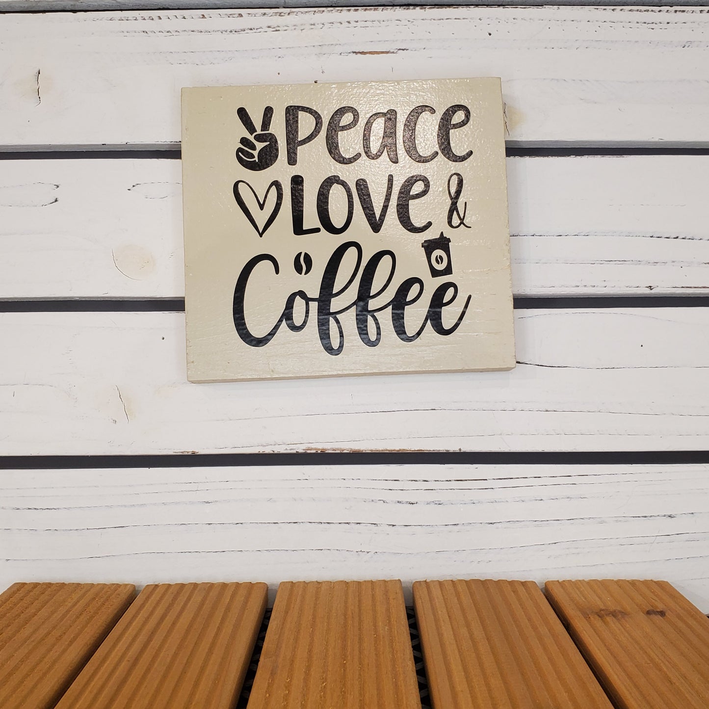Decorative sign with 'Peace Love & Coffee' text on a wooden surface.