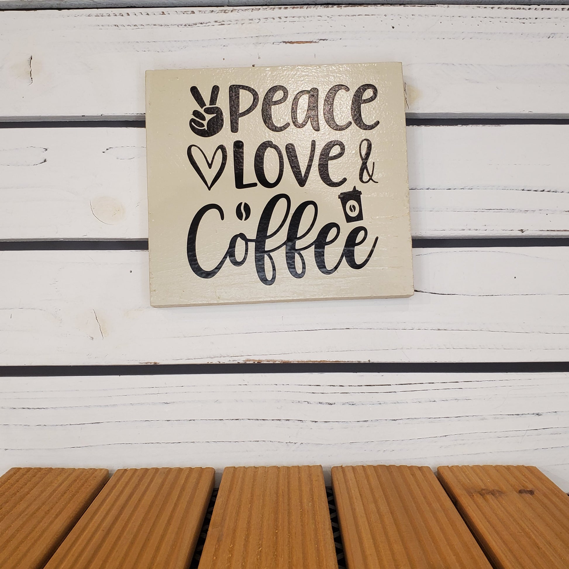 Decorative sign with 'Peace Love & Coffee' text on a wooden surface.
