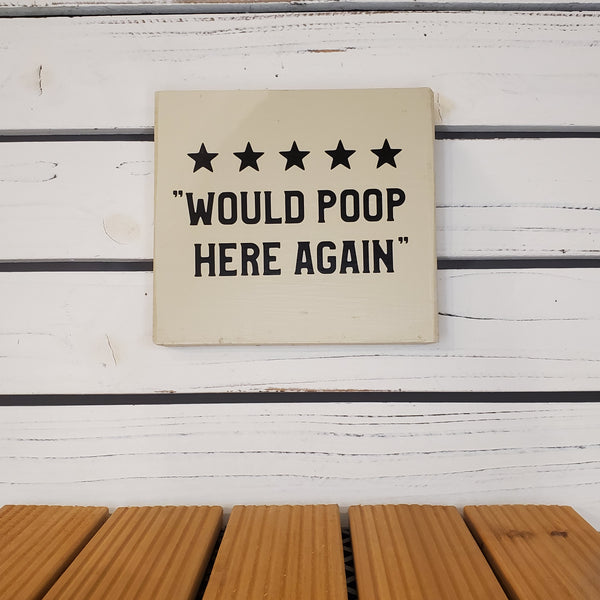Beige sign with text 'WOULD POOP HERE AGAIN' on a wooden surface