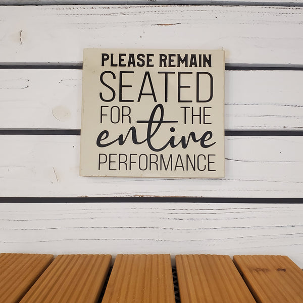 Sign on a white wooden door with text 'Please remain seated for the entire performance'.