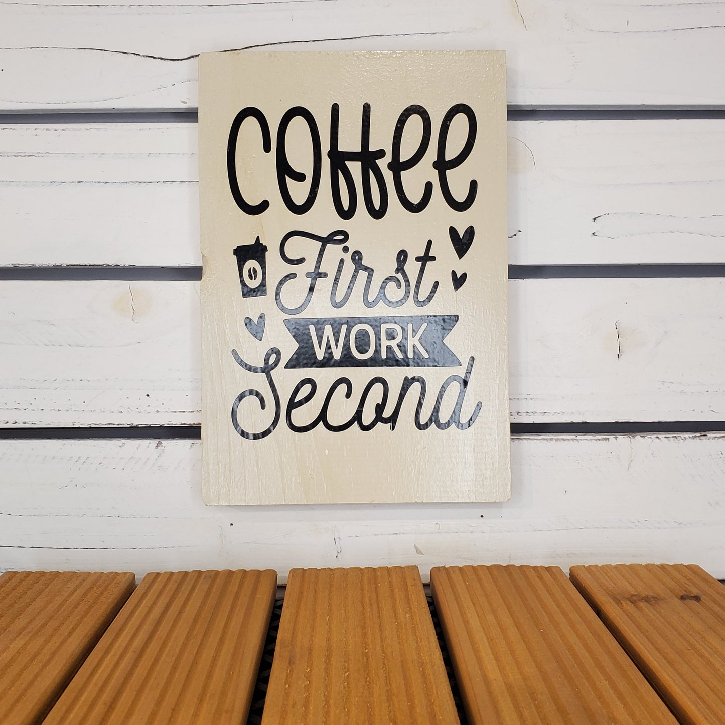 Decorative sign with 'Coffee First, Work Second' text on a wooden surface.