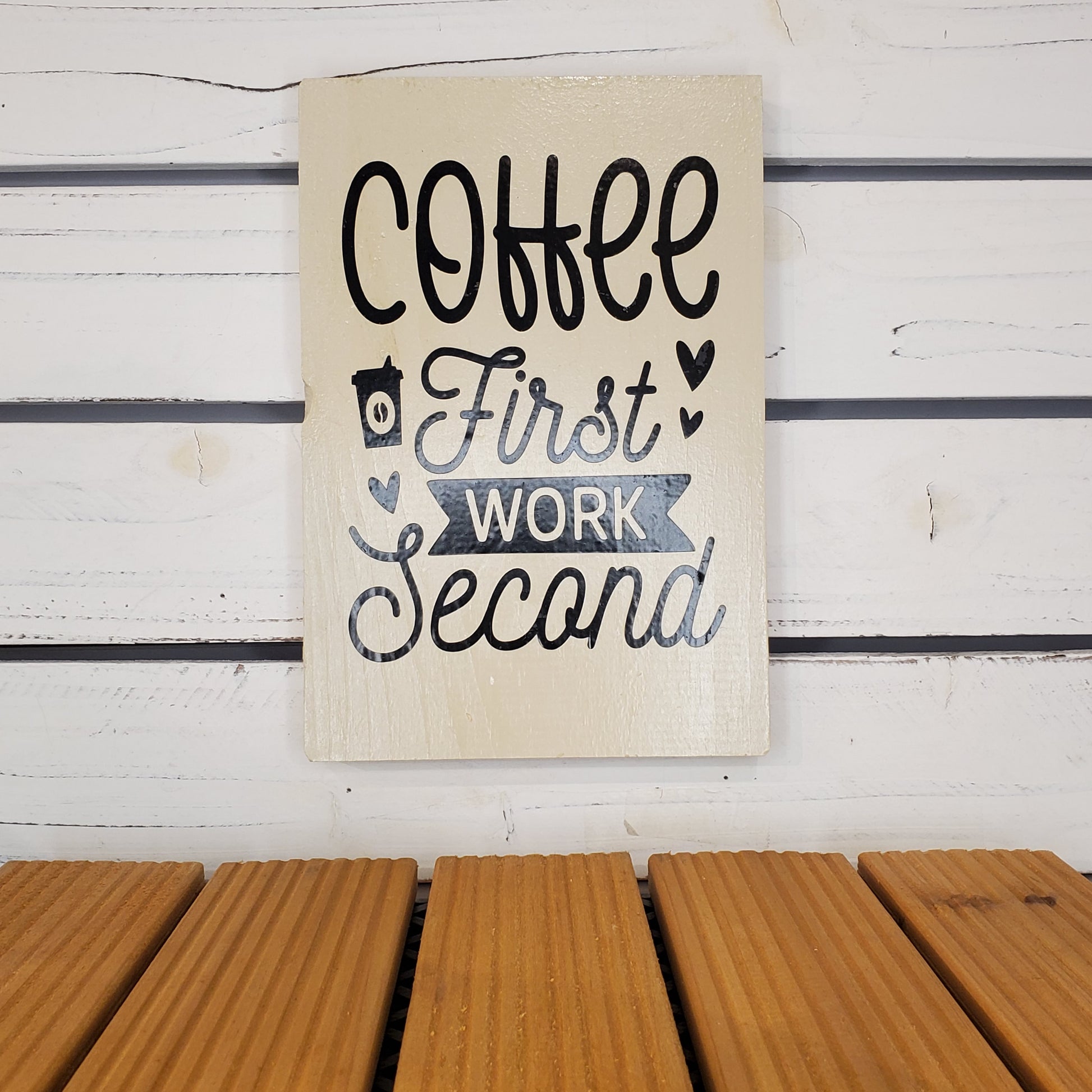 Decorative sign with 'Coffee First, Work Second' text on a wooden surface.