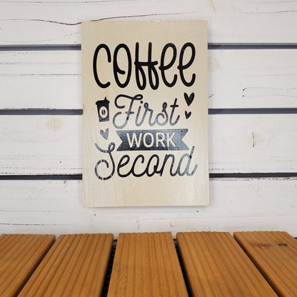 Decorative sign with 'Coffee First, Work Second' text on a wooden surface.