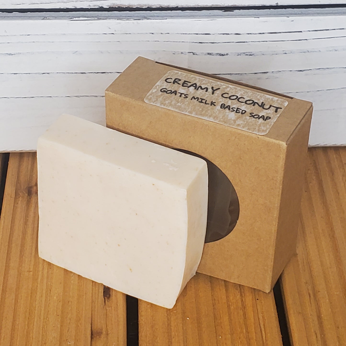 Bar of soap with a cardboard box labeled 'Creamy Coconut' on a wooden surface.
