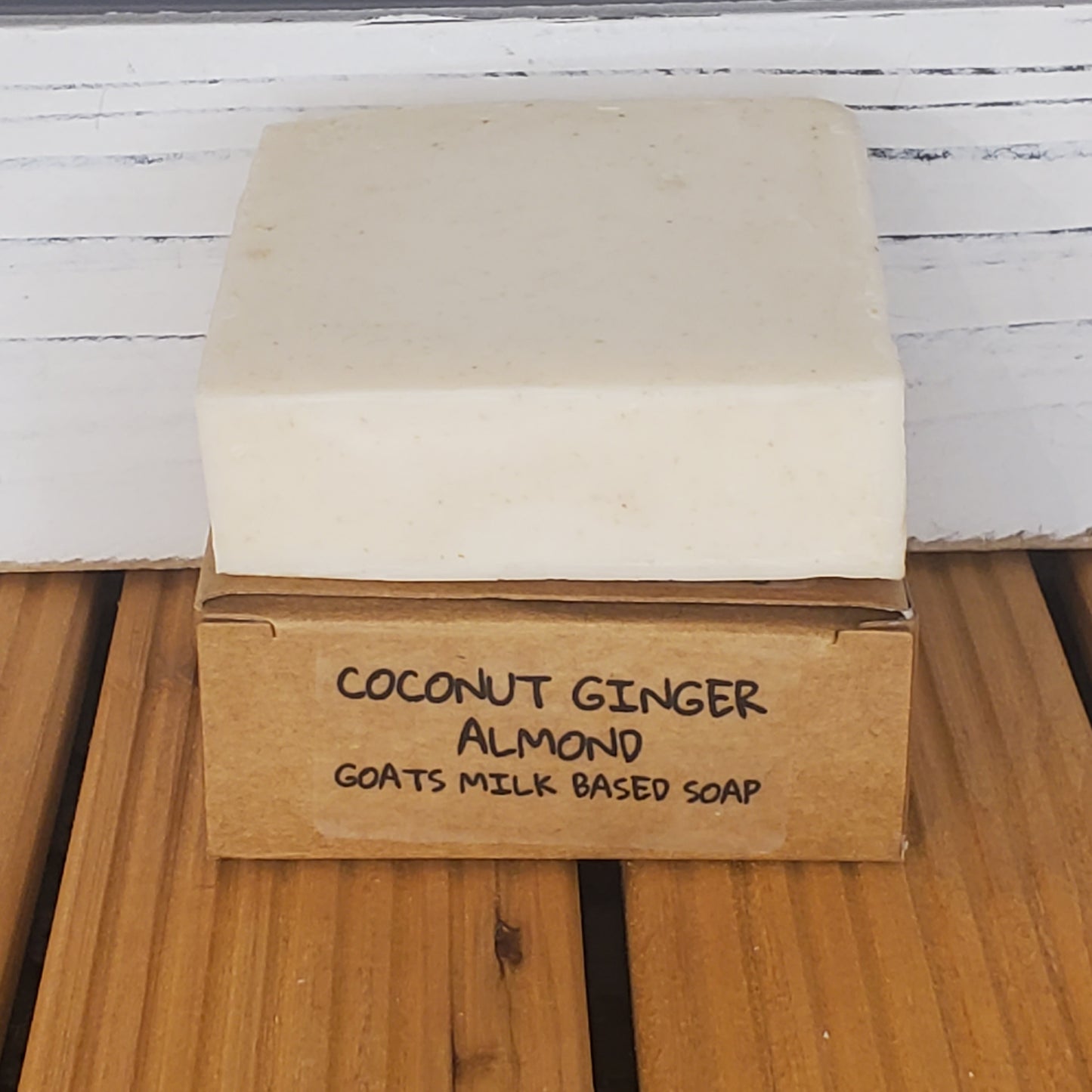 Bar of soap with a cardboard box labeled 'Coconut Ginger Almond Goats Milk' on a wooden surface.