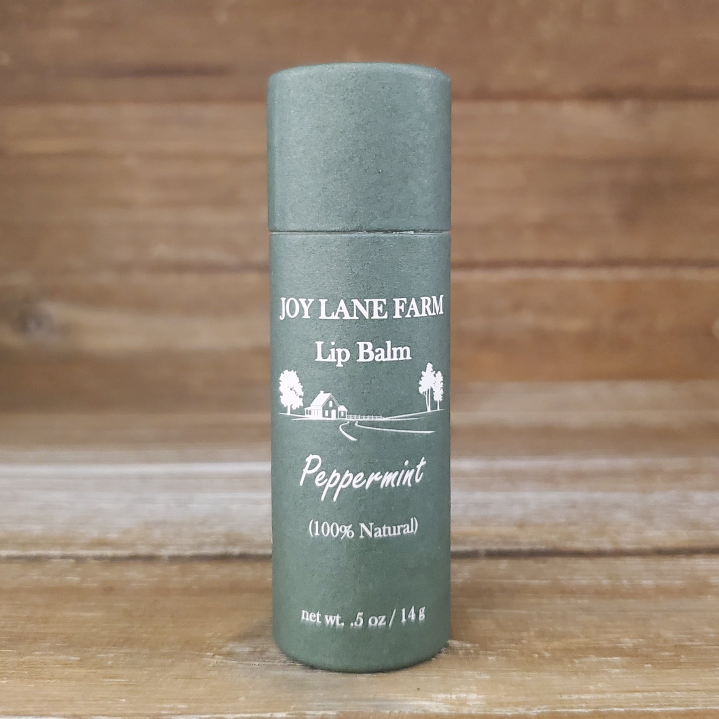 Lip balm container with 'Joy Lane Farm' branding on a wooden background